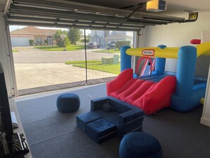 Una habitación con un trampolín, un tobogán y vistas a un barrio residencial a través de la puerta del garaje.