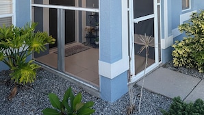 Ein Haus mit überdachter Terrasse, einer Schiebetür und einem kleinen Garten mit Pflanzen.