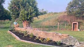 Un jardin avec un chemin en briques, un arbre et une petite construction en bois.