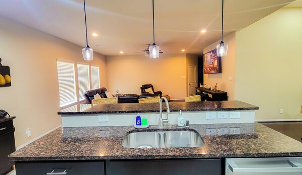 A kitchen with granite countertops, a double sink, and pendant lighting.