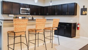 A kitchen with dark cabinets, a microwave, and three wicker bar stools. - Home In The Heart Of Alvin! (Alvin)
