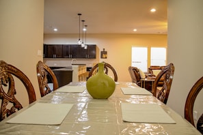 A dining area with a table set for four, surrounded by wooden chairs. A green vase is placed in the center of the table.