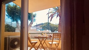 Un espace extérieur aménagé avec une table et des chaises, un ventilateur, et une vue sur le paysage environnant, notamment les arbres et les bâtiments.