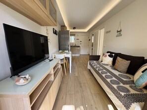A modern living room with a flat-screen TV, a sofa, and a dining area with a table and chairs. - On the Beach Holiday Home (Los Cristianos)