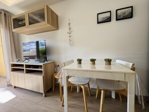 A dining area with a white table, wooden chairs, a TV on a wooden cabinet, and two framed pictures on the wall. - On the Beach Holiday Home (Los Cristianos)