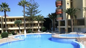 Une piscine entourée de palmiers et un immeuble à plusieurs étages doté de balcons.