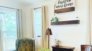 A dining area with a wooden table, two chairs, a floral armchair, a vase with flowers, and a wall sign. - Cozy Lakeview Cabin, Boat Parking, Breathtaking Lake View, One Hour from Tulsa  (Afton)