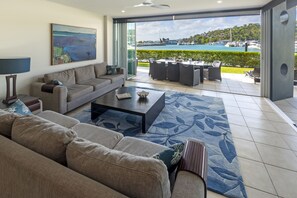 A modern living room with a sofa, coffee table, and a view of a marina through large glass doors. - Pavillions 21  (Hamilton Island)