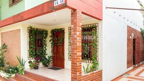 A two-story building with a red brick entrance, a wooden door, and a balcony with potted plants.