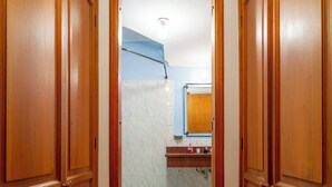 A hallway with wooden doors leading to a bathroom with a marble floor and a blue shower curtain.