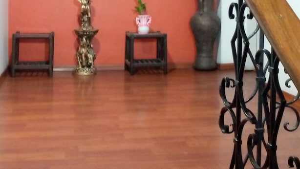 A room with a wooden floor, a large abstract painting on the wall, a statue, a vase with flowers, and a staircase with a wooden handrail. - The Imperial Hostal (Quito)