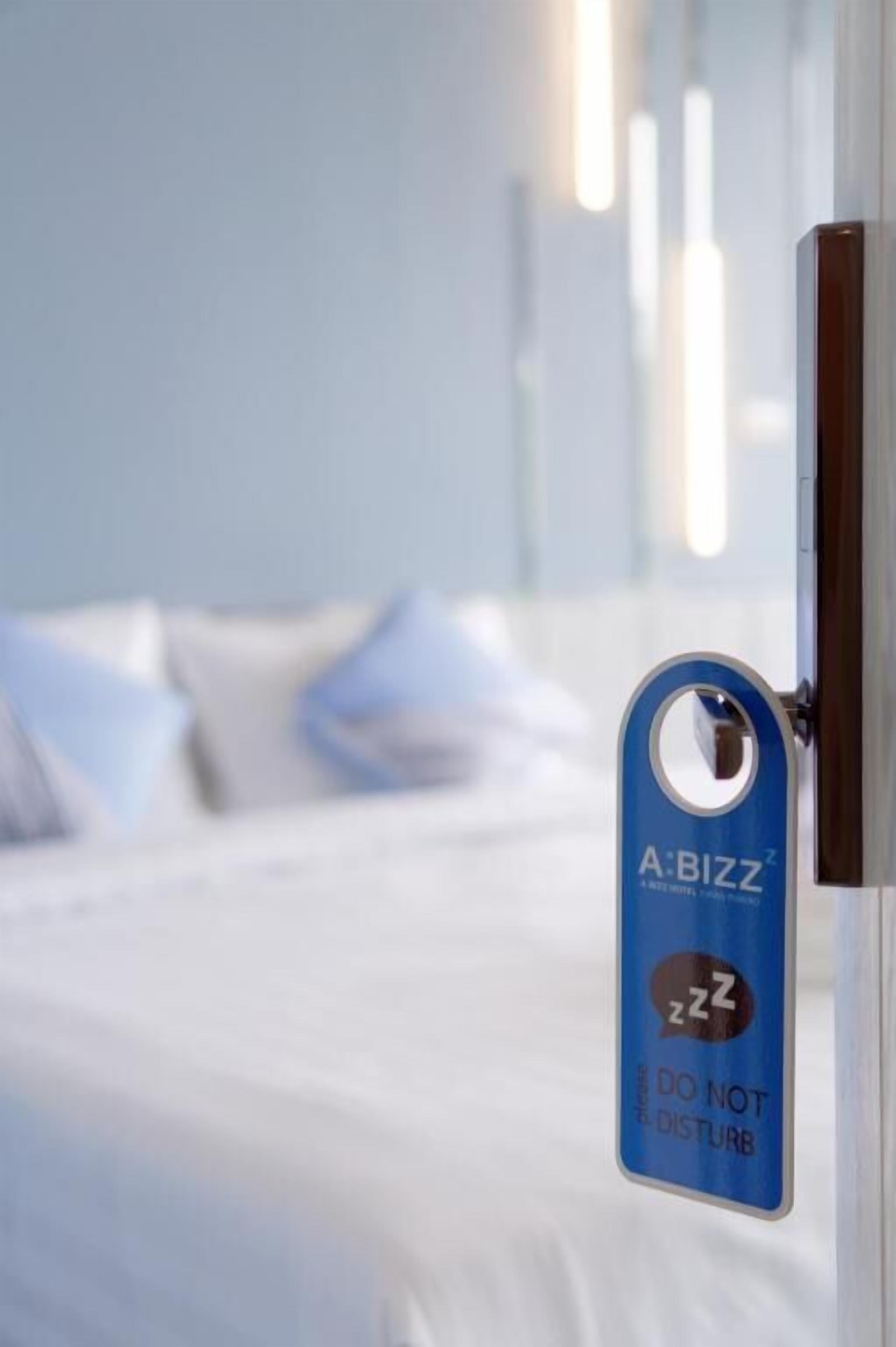 Une chambre d’hôtel avec un lit, des oreillers et une pancarte sur la porte indiquant : « A : NE PAS DÉRANGER. »