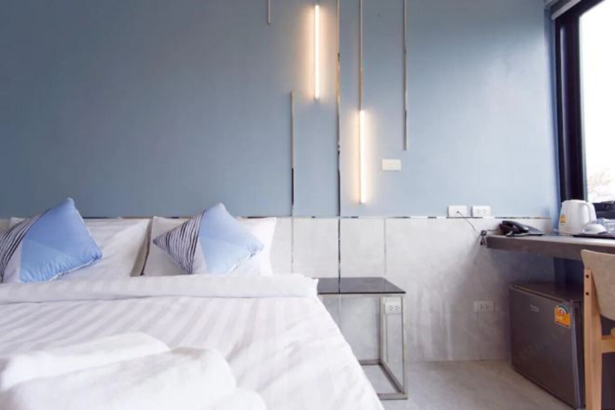 Een moderne hotelkamer met een bed, nachtkastje, bureau en een kleine kitchenette.