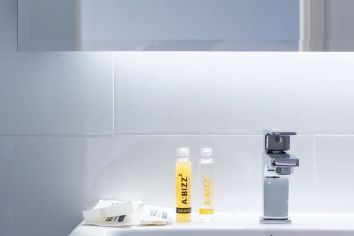 Une salle de bain avec un lavabo blanc, deux bouteilles jaunes étiquetées « A:BIZZ » et un robinet argenté.