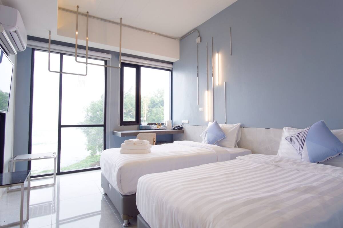 Une chambre d’hôtel moderne, dotée de deux lits, d’un bureau et d’une grande fenêtre donnant sur l’extérieur.