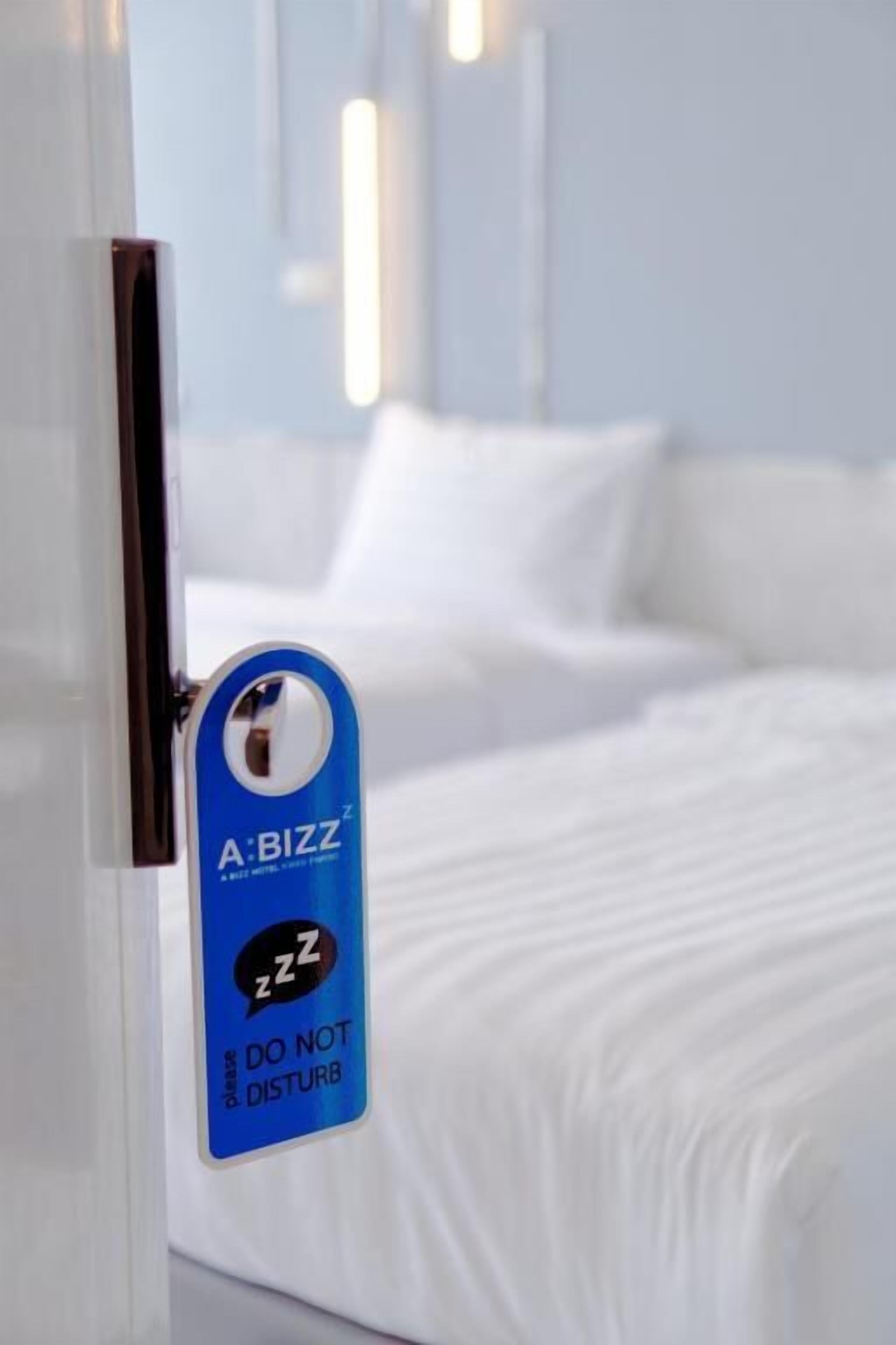 A hotel room with a bed, a door with a blue keycard that reads "A BIZZ" and "DO NOT DISTURB".