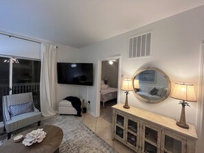 A modern living room with a flat-screen TV, a sofa, a coffee table, and a console table with lamps.