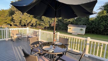 Une terrasse avec une table ronde et des chaises, un parasol et une clôture blanche.