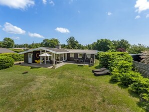 Et moderne hus med en overdækket terrasse, græsplæne og have.