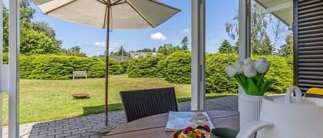 A patio with a table, a magazine, a basket of cupcakes, and a vase of flowers.