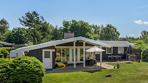 Una casa moderna con un porche cubierto, un tobogán amarillo y un césped bien cuidado.