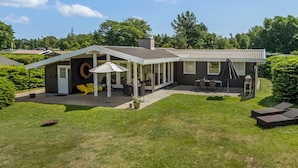 Una casa moderna con un patio cubierto, mobiliario exterior y un césped bien cuidado.