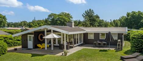 A modern house with a covered patio, outdoor seating, and a well-maintained lawn.