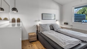 Un dormitorio moderno con cama, mesitas de noche, ventana con vistas y techo con vigas a la vista.