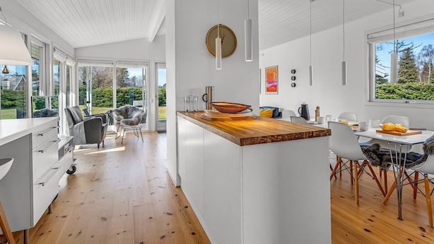 Una cocina moderna con isla de madera, armarios blancos y un amplio ventanal con vistas al exterior.