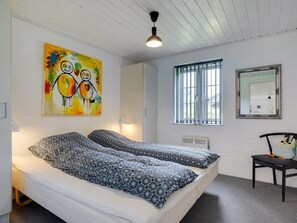 Ein Schlafzimmer mit zwei Betten, einem Fenster mit Gitterstäben, einem Spiegel und einem Bild an der Wand.
