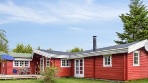 Een rode houten woning met schoorsteen, een veranda met tafel en stoelen, en een gazon.