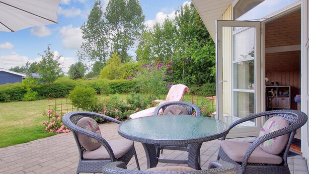 An outdoor patio with wicker furniture, a glass table, and a view of a garden with trees and flowers. - "Lilia" - 900m from the sea by Interhome (Væggerløse)