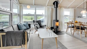 Een moderne woonkamer met een groot raam, een bank, een tafel en een zwarte houtkachel.