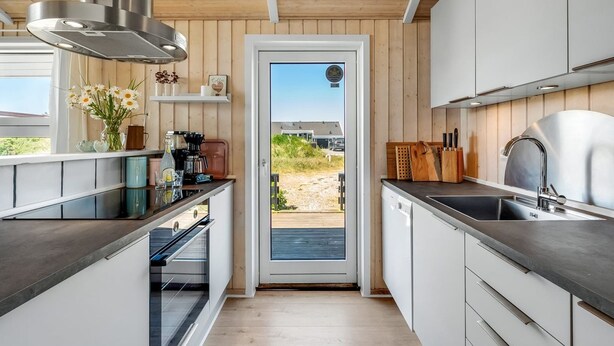 Een moderne keuken met houten lambrisering, een inbouwoven, een koffiehoek en uitzicht door een glazen deur.
