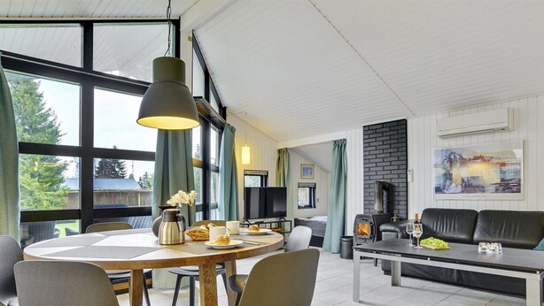 A modern living room with a round dining table, comfortable seating, a fireplace, and large windows offering a view of the outdoors. - "Aimi" - 270m from the sea by Interhome (Væggerløse)