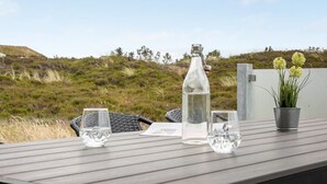 Une table avec une bouteille, des verres et une plante en pot, sur une terrasse offrant une vue sur un paysage verdoyant.