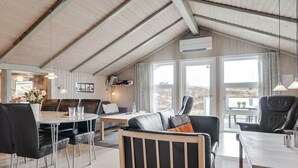 Une pièce spacieuse avec un plafond haut, un coin repas avec une table et des chaises, un canapé avec des coussins et une grande fenêtre donnant sur un paysage agréable.