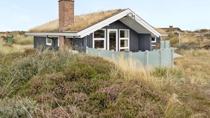 Une maison moderne avec un toit végétalisé, de grandes fenêtres et une cheminée en briques.