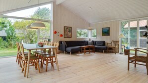 Een ruime woonkamer met een eethoek, grote ramen en uitzicht op de omgeving.