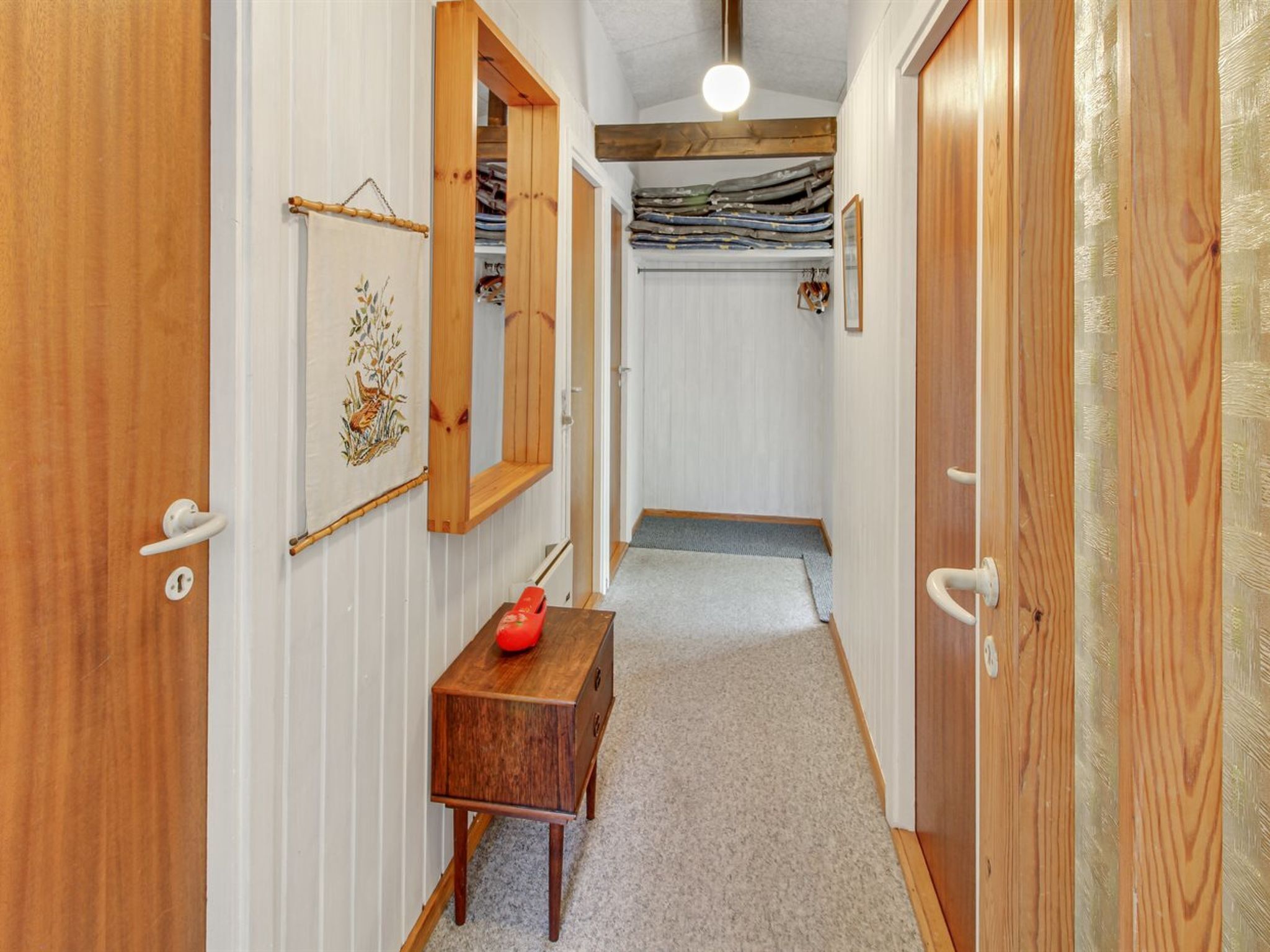 Un pasillo estrecho con puertas de madera y una pequeña mesa de madera con un objeto rojo encima.