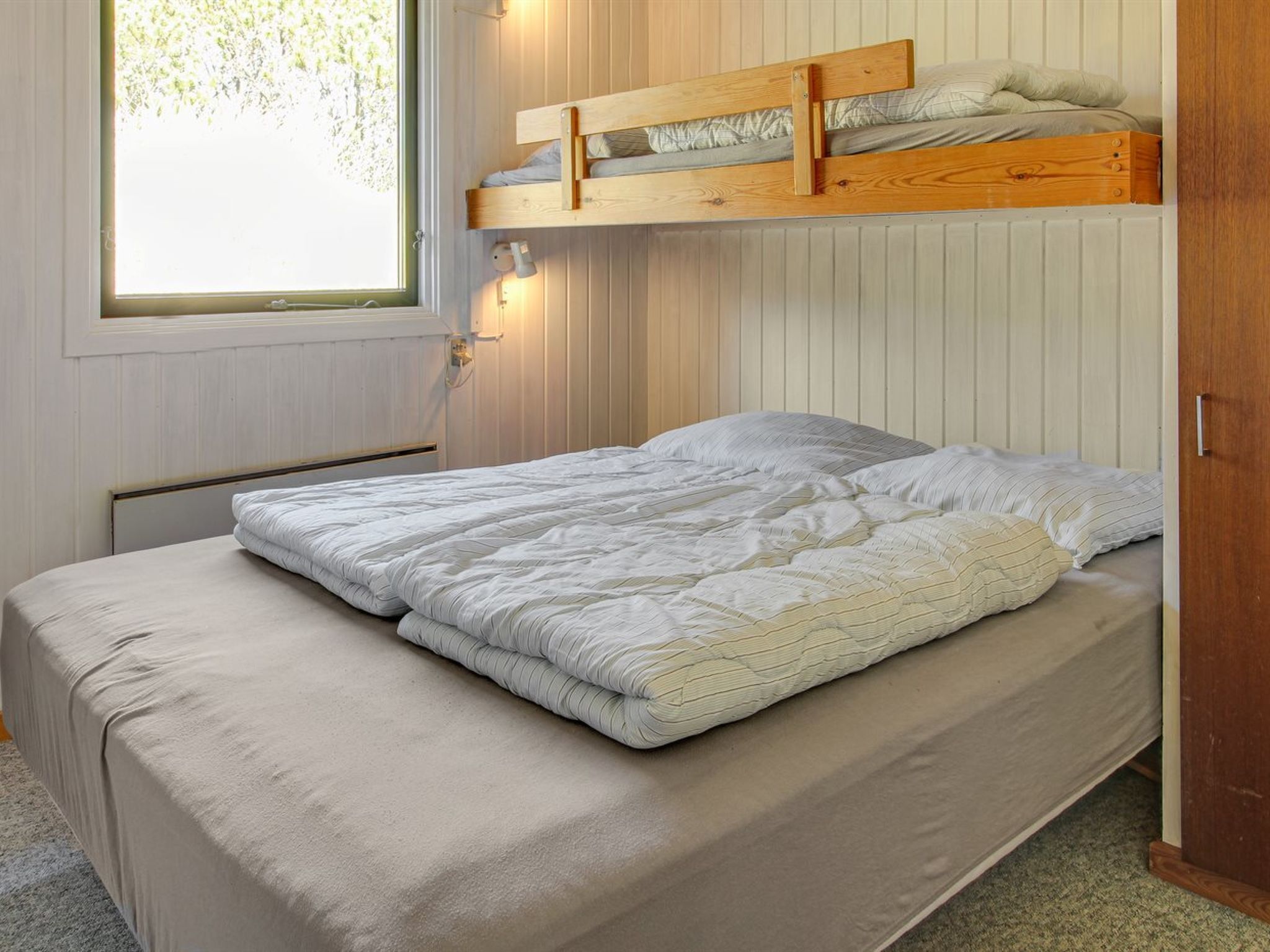Een enkel bed met een houten hoofdbord, een raam met uitzicht op bomen en een wandlamp.