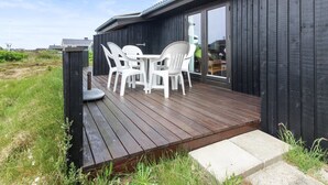 A wooden deck with a table and chairs, a black exterior wall, and a glass door leading inside. - "Svenne" - 500m from the sea by Interhome (Ringkøbing)