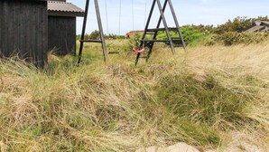 A wooden swing set in a grassy field with a wooden structure in the background. - "Svenne" - 500m from the sea by Interhome (Ringkøbing)
