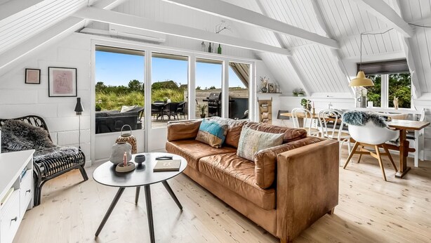 Un loft spacieux avec de hauts plafonds, de grandes fenêtres, un coin salon confortable avec un canapé en cuir et un coin repas avec une table et des chaises en bois.