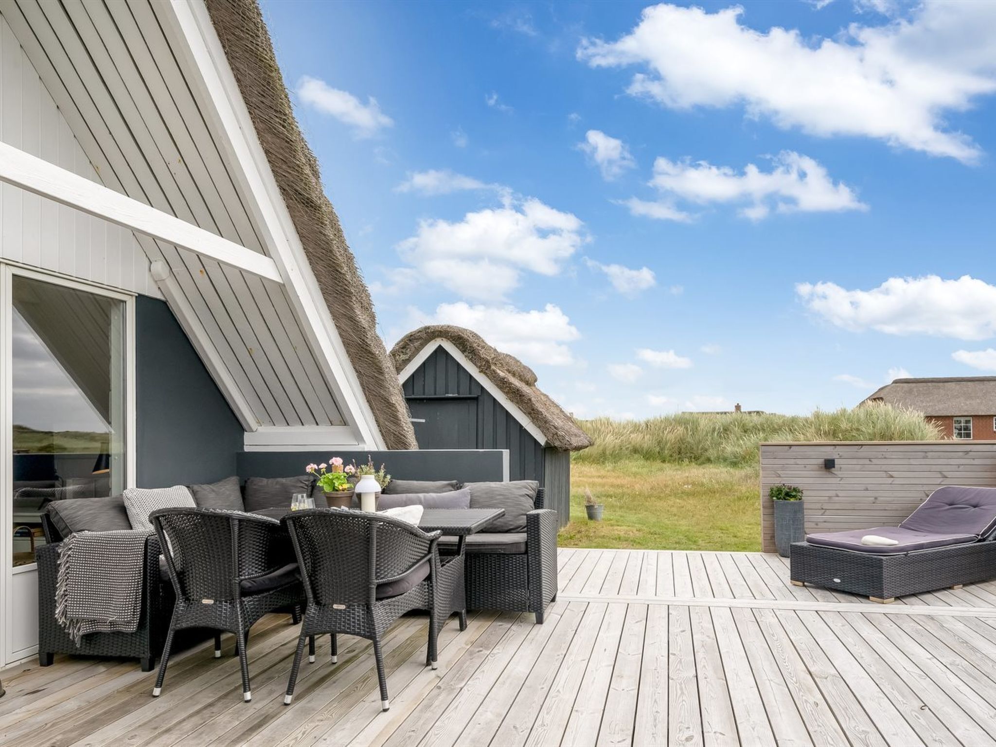 Een modern buitenterras met een eethoek, een zithoek en een constructie met rieten dak.