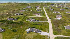 Vue aérienne d’un village côtier avec ses maisons traditionnelles aux toits de chaume, une route principale et l’océan en arrière-plan.