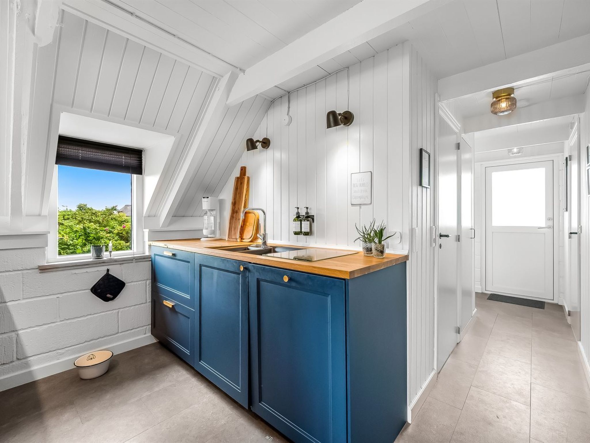 A modern kitchen with a wooden countertop, blue cabinets, and a window with a view of greenery.