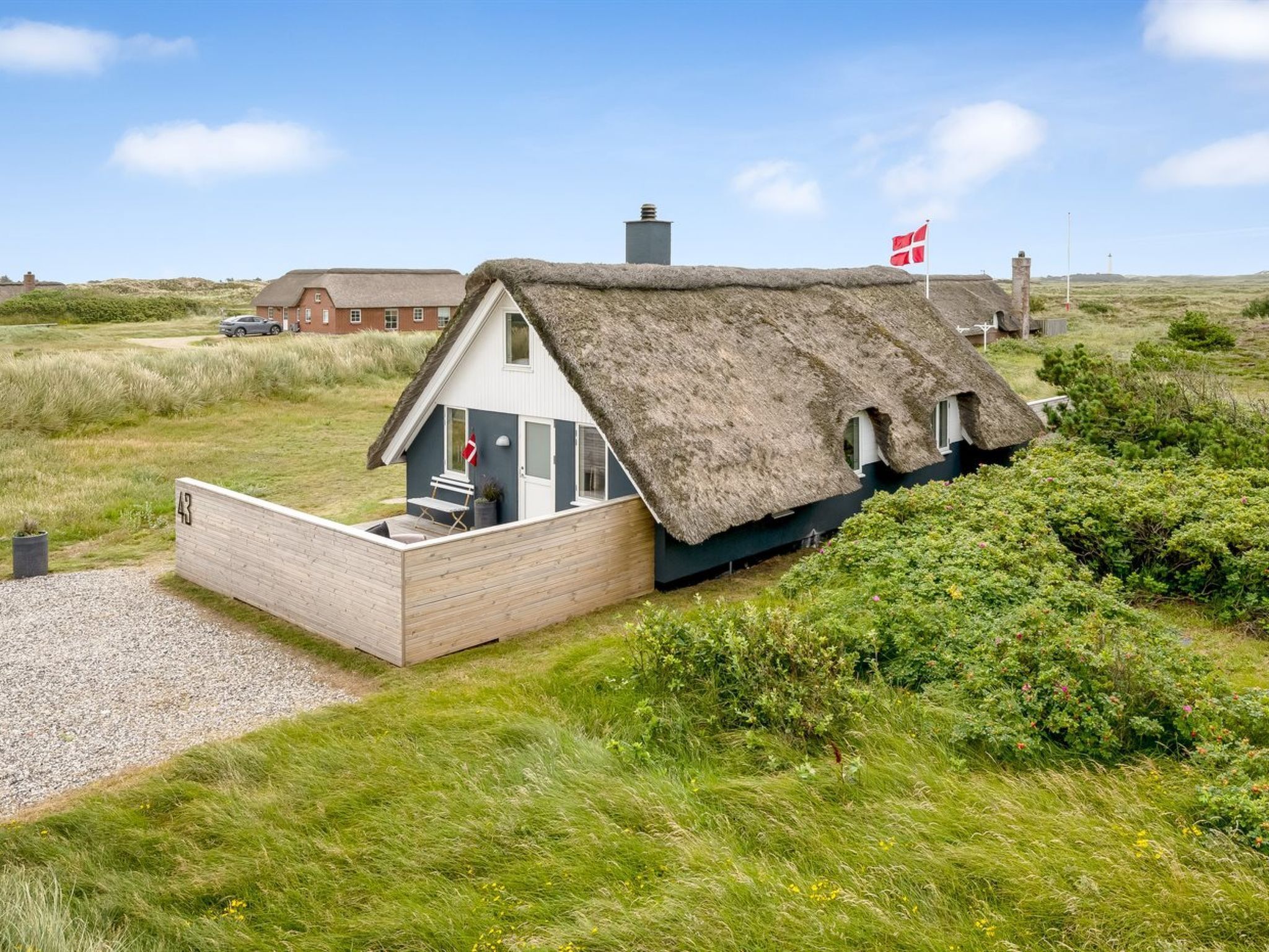 Een rieten huis met een klein terras en een vlag, omgeven door groen.