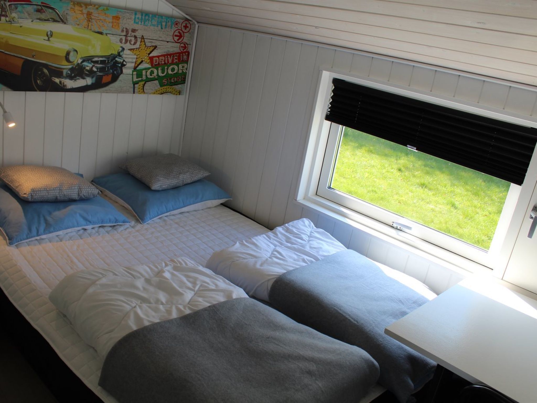 A bedroom with two beds, a window with blinds, and a wall mural advertising a liquor store.
