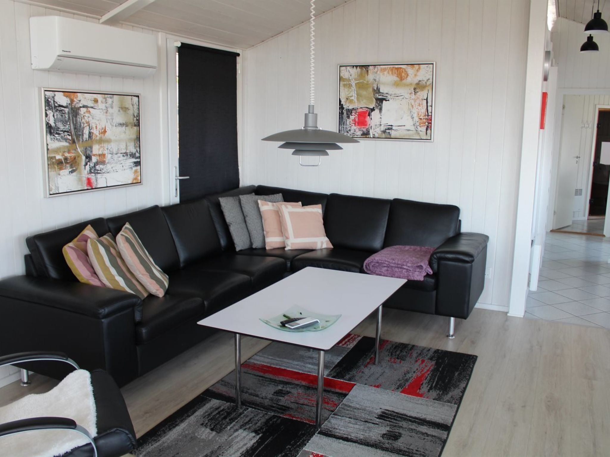 Un salon moderne avec un canapé en cuir noir, une table basse blanche et des œuvres d’art abstraites accrochées aux murs.